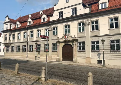 Bischhofshaus. Altes Gebäude, das schön verziert ist, davor Straßenbahnschienen auf Pflastersteinen.